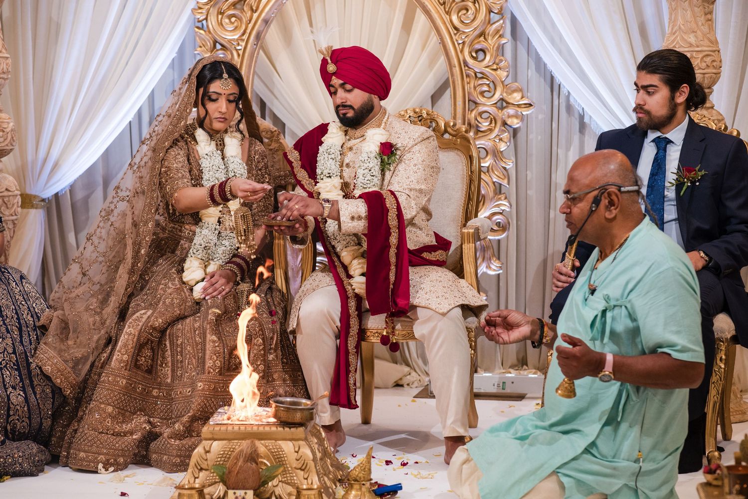Sikh bride and groom performing traditional wedding rituals beside sacred fire with priest.