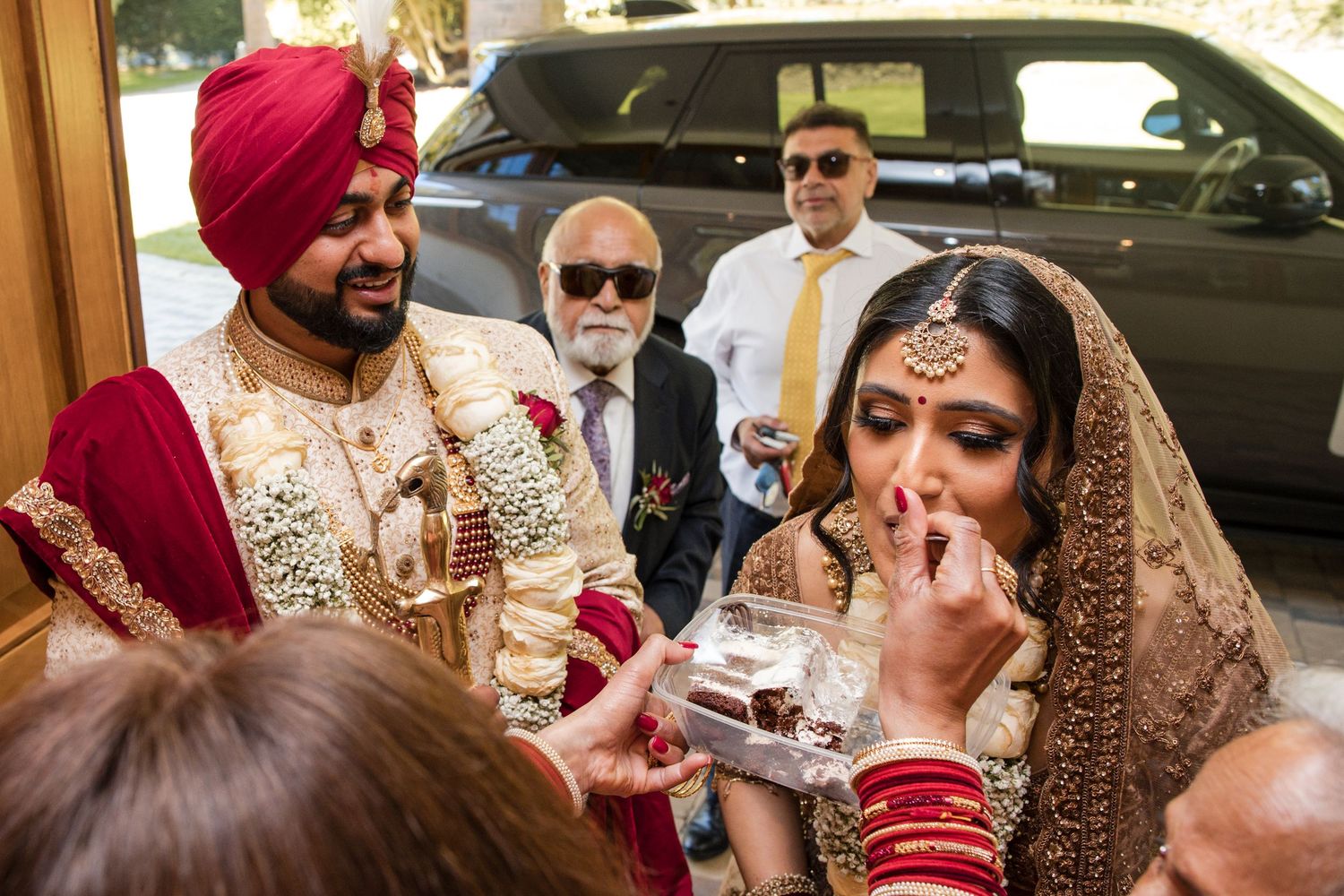 Sikh bride in gold lehenga receiving sweets during traditional wedding welcome ceremony outdoors.