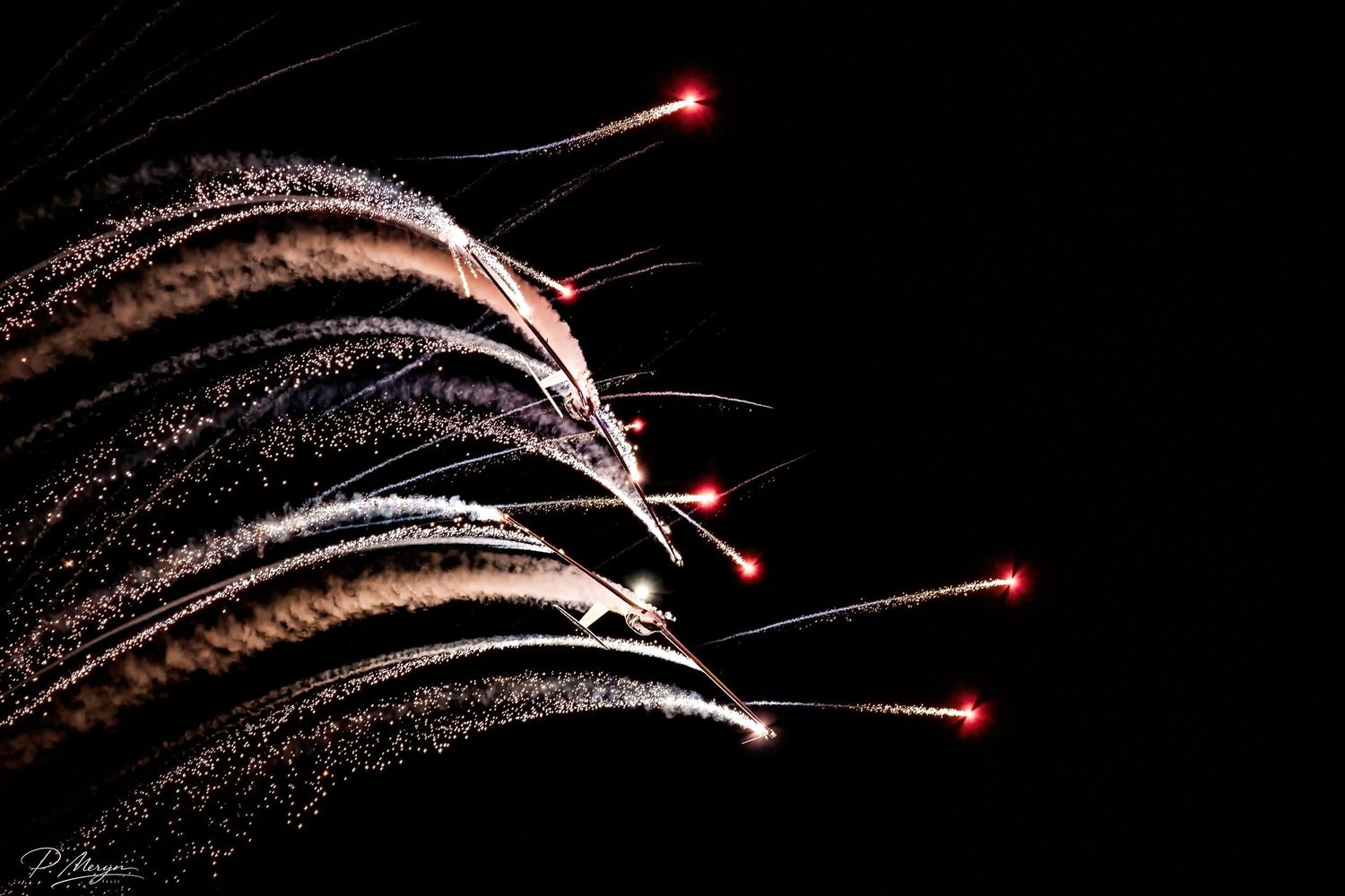 Colorful fireworks with glowing red tips streak across a dark night sky in a dramatic display.