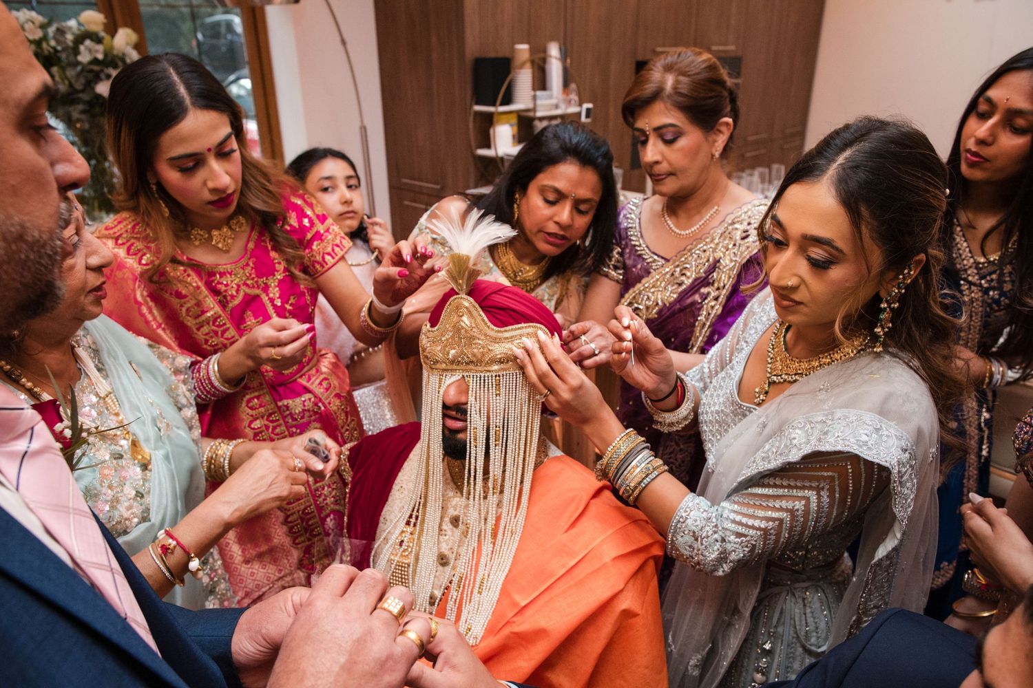 Family members help a bride with her traditional Indian wedding headpiece during bridal preparations.