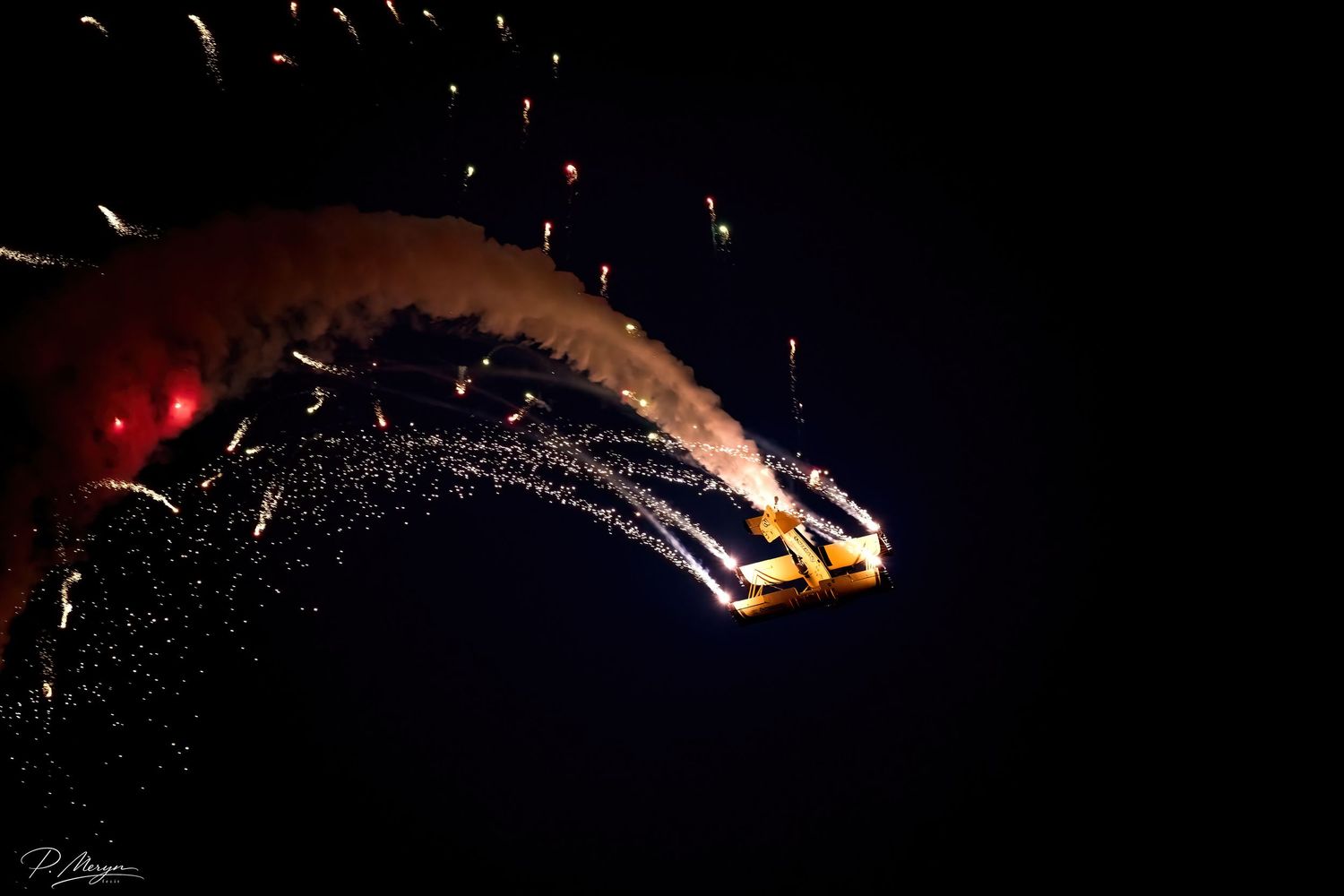 Aircraft releasing dramatic pyrotechnic sparks display during nighttime airshow performance.