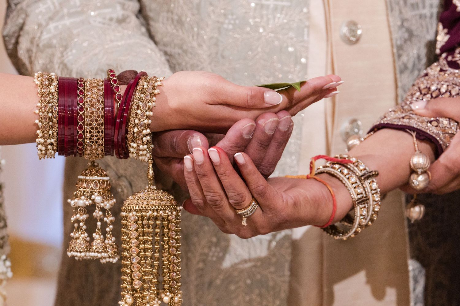 Close-up of hands exchanging rings with ornate gold and red bangles at South Asian wedding.
