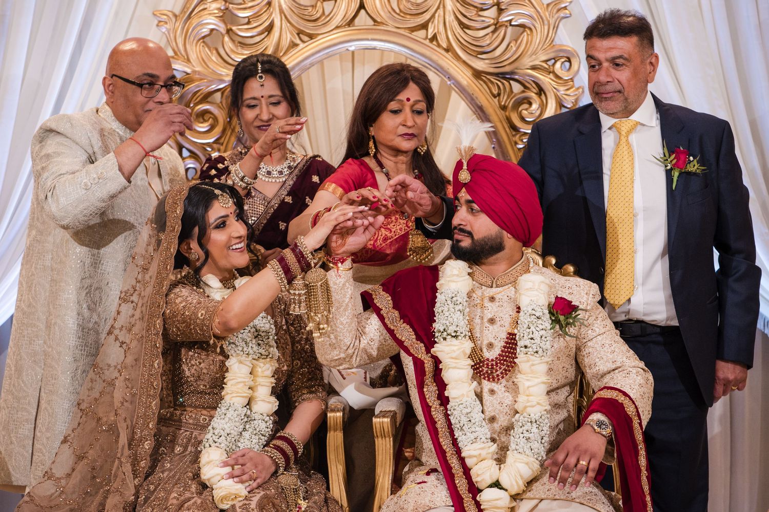 South Asian family gathering around bride and groom at traditional Sikh wedding ceremony.