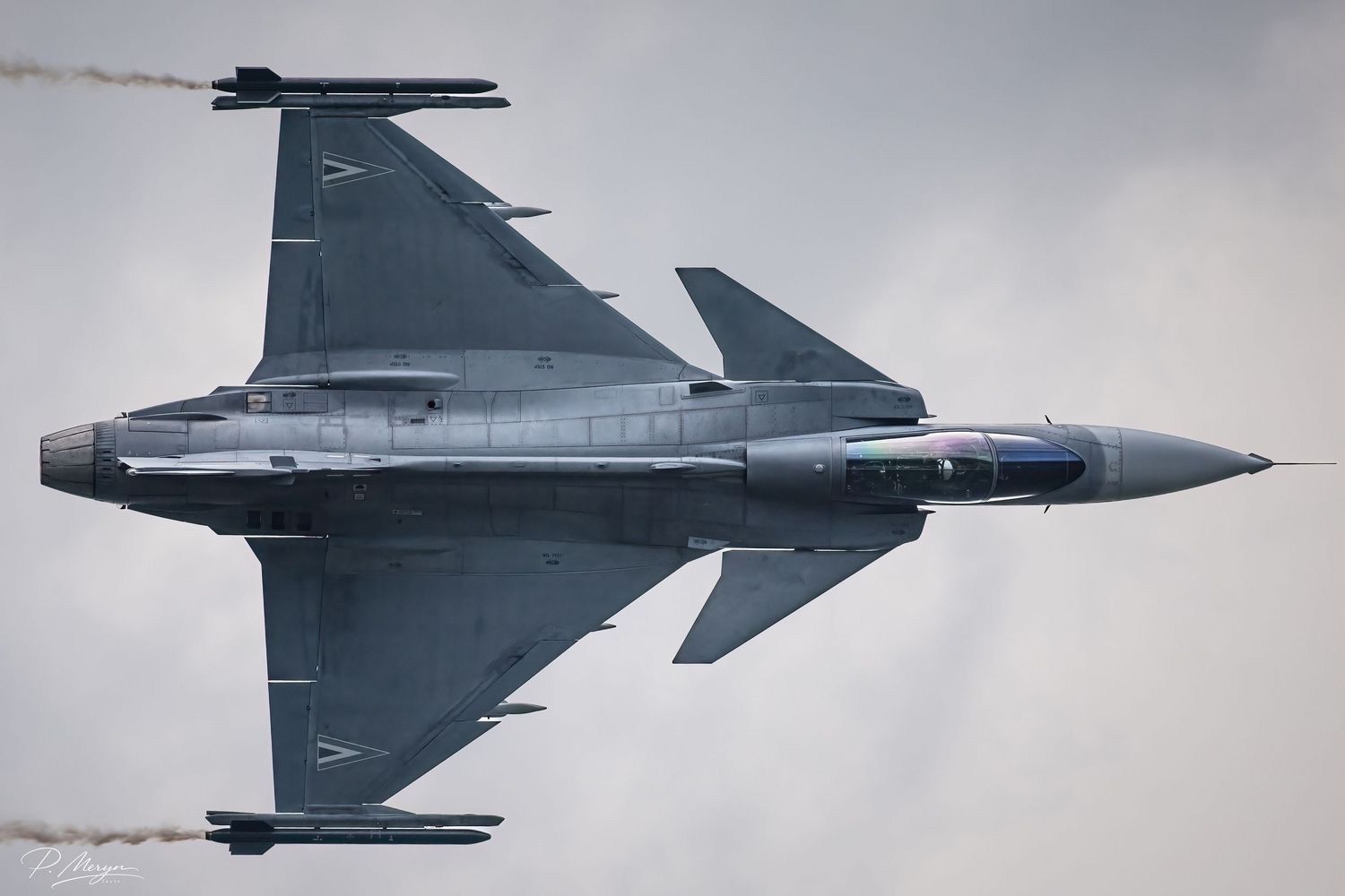 Bottom view of Saab Gripen fighter jet performing high-speed pass at airshow.