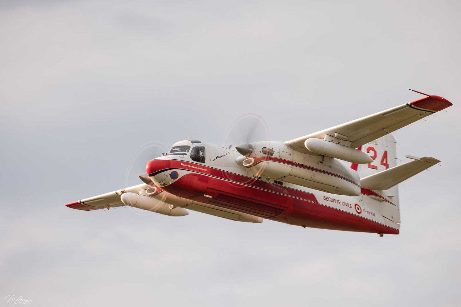 A red and white twin-engine aircraft numbered 24 flying against an overcast sky at an airshow.