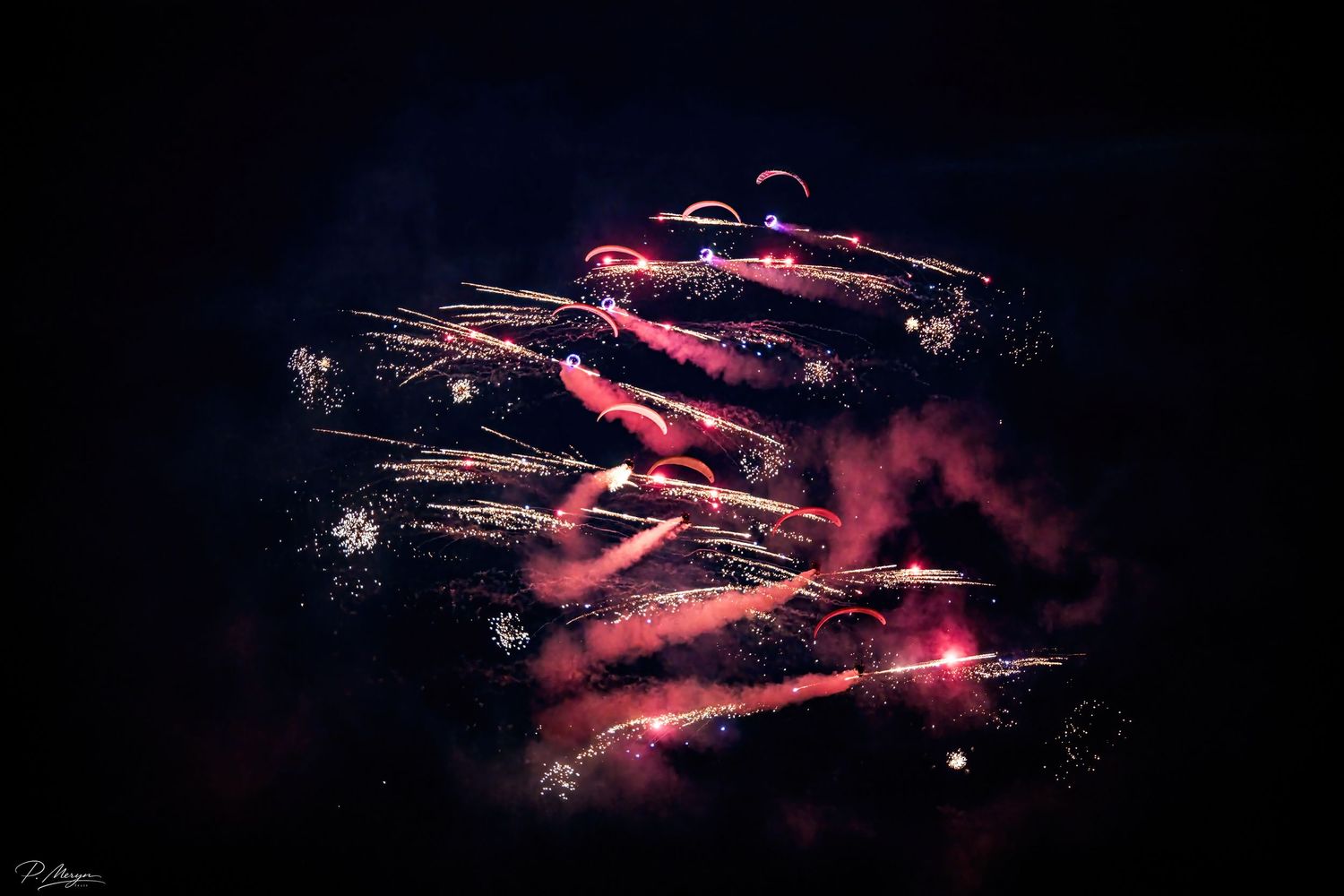 Spectacular nighttime fireworks display with red and pink bursts against a dark sky.