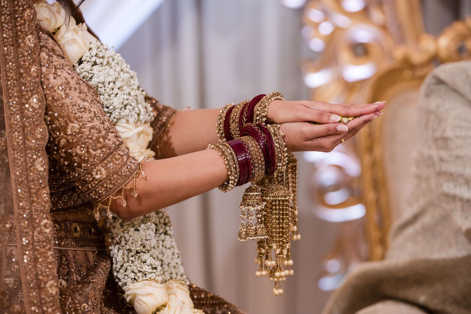 Bride wearing traditional South Asian gold and red bangles and bridal jewelry at wedding.