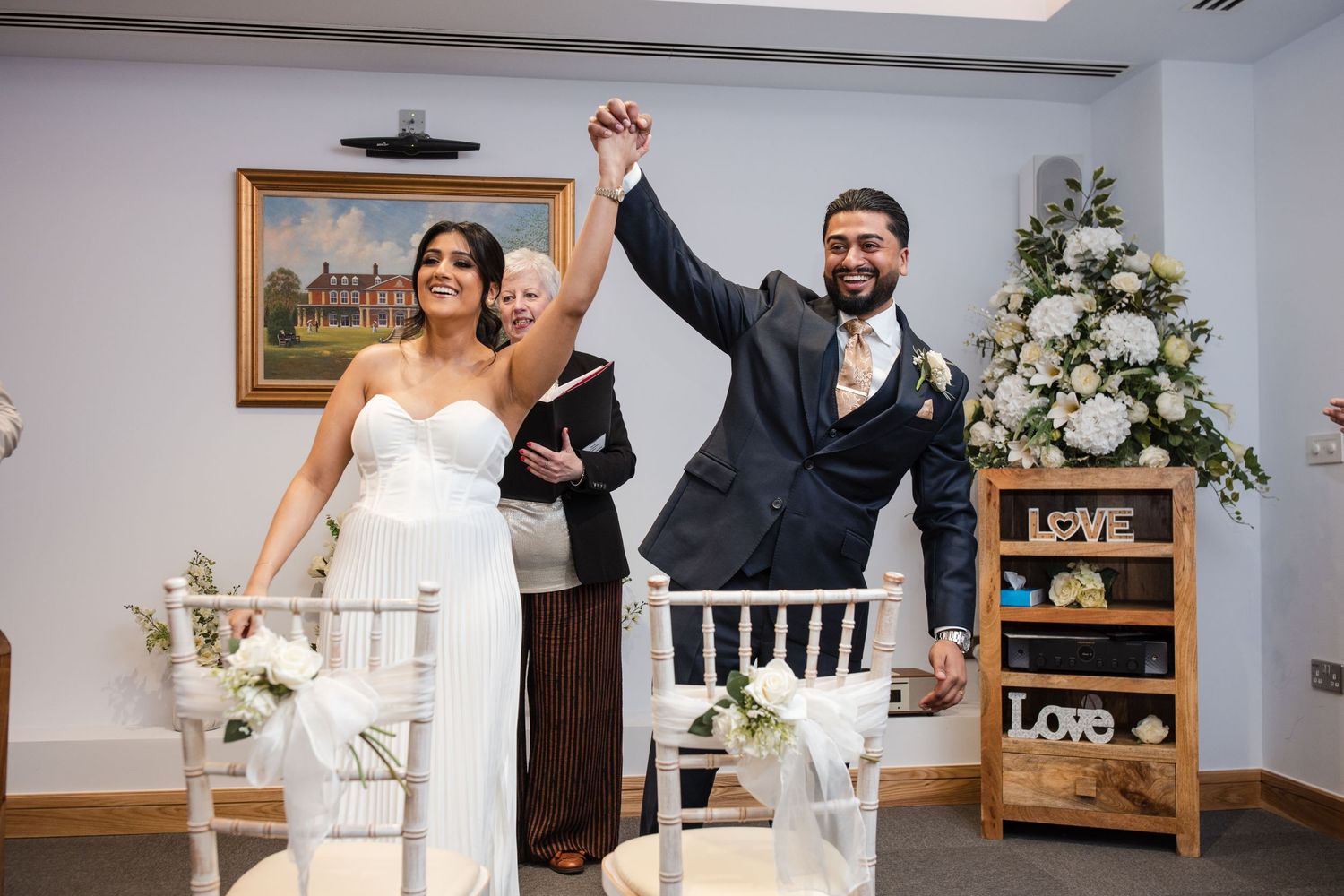 Bride and groom raising hands in celebration at wedding ceremony with floral decorations.