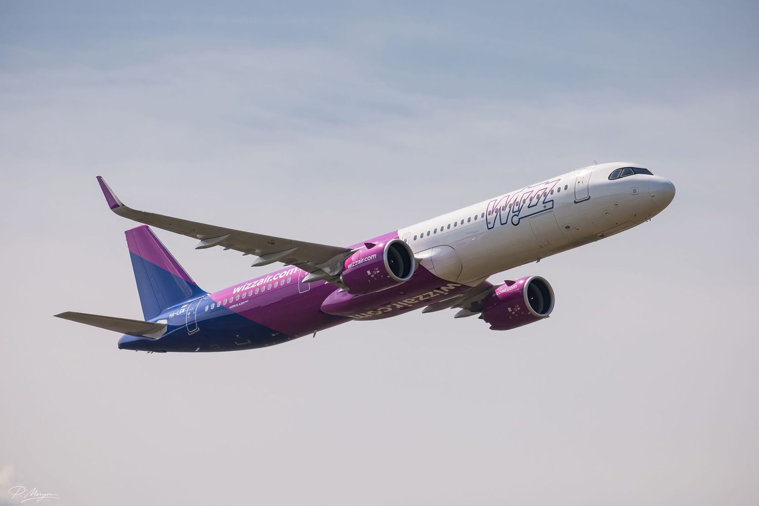 Wizz Air Airbus A321neo in pink and white livery climbing steeply after takeoff against a cloudy sky.