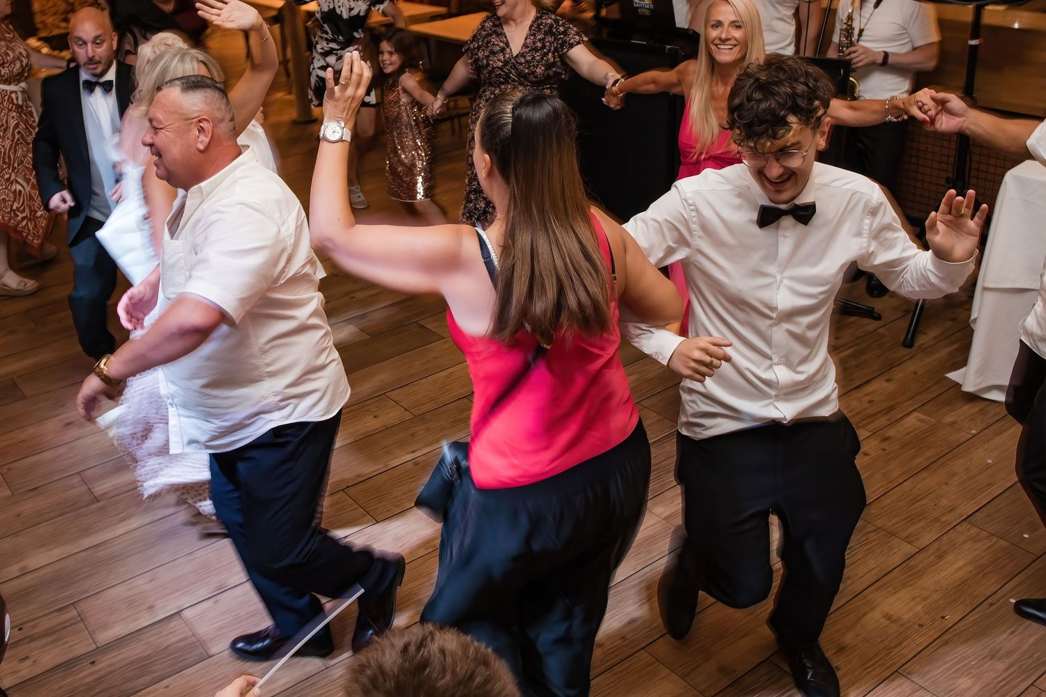 Wedding guests energetically dance together on wooden dance floor during lively wedding reception celebration.
