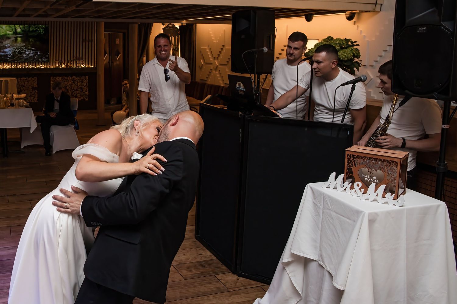 Groom dips bride dramatically on dance floor during wedding reception while band performs in background.