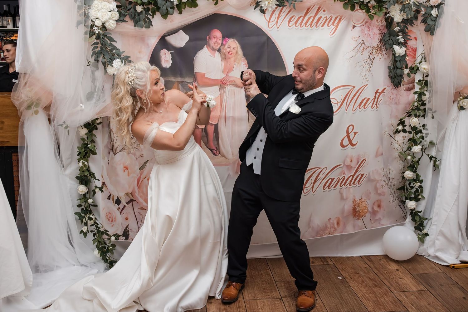 Bride and groom dance joyfully in front of a personalized wedding backdrop reading Matt and Wanda.