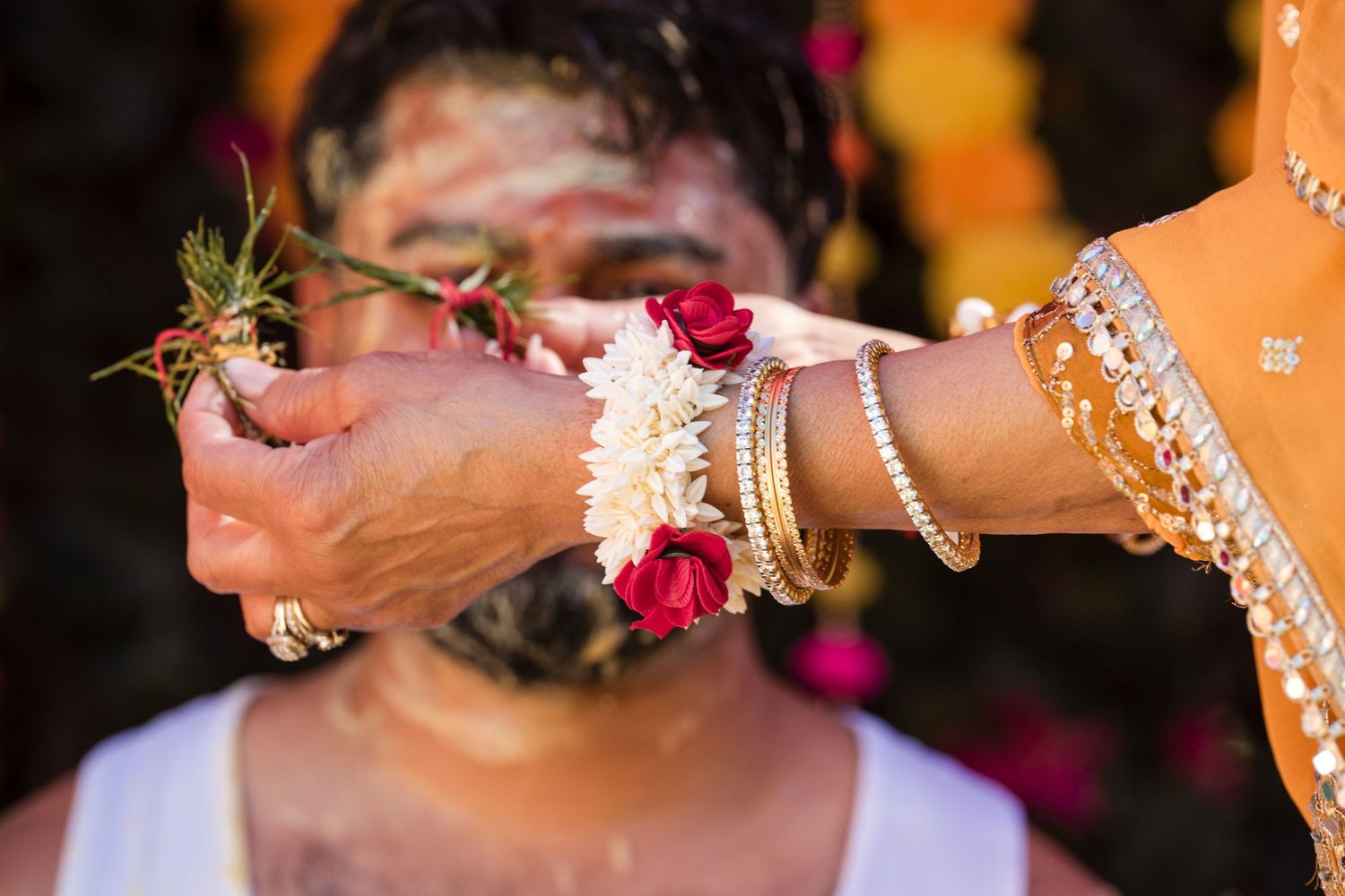 Close-up of hands applying haldi turmeric paste with red and white flowers during Indian wedding ceremony.