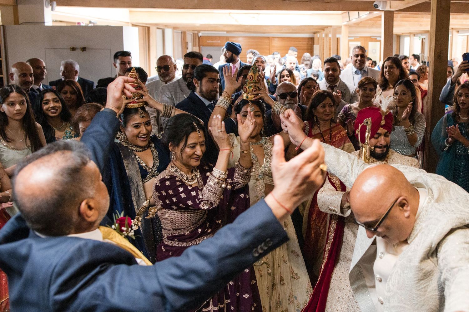 Guests celebrate with raised hands as a bride in traditional Indian attire walks through a crowd.