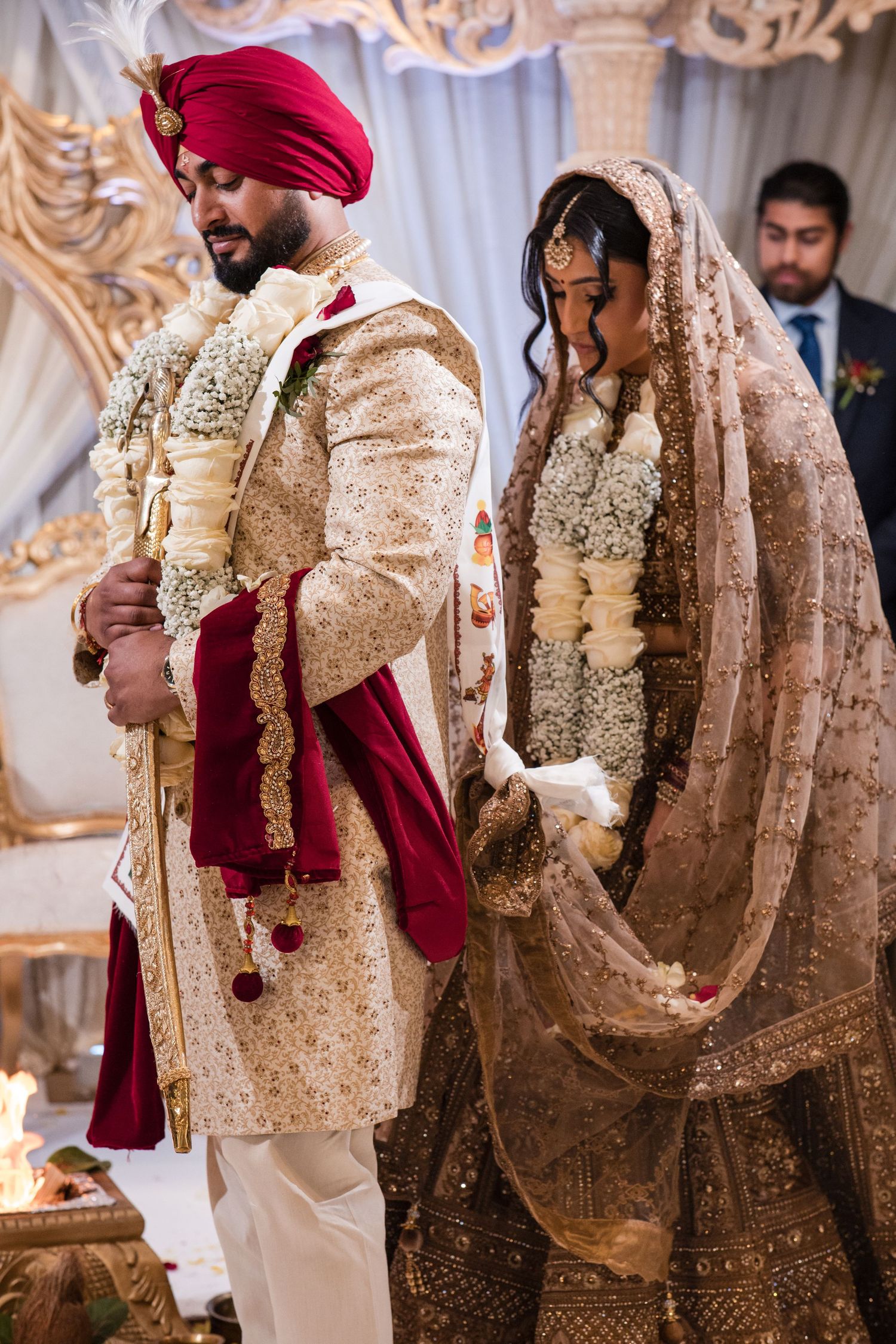 Sikh bride and groom performing wedding ceremony rituals in traditional gold and red attire with floral garlands.
