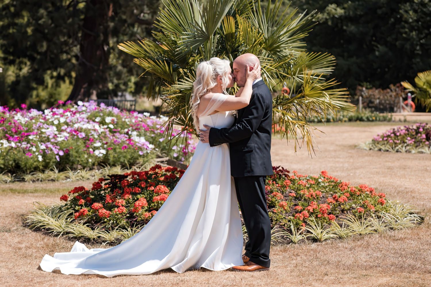Bride and groom share a romantic kiss surrounded by colorful garden flowers on their wedding day.