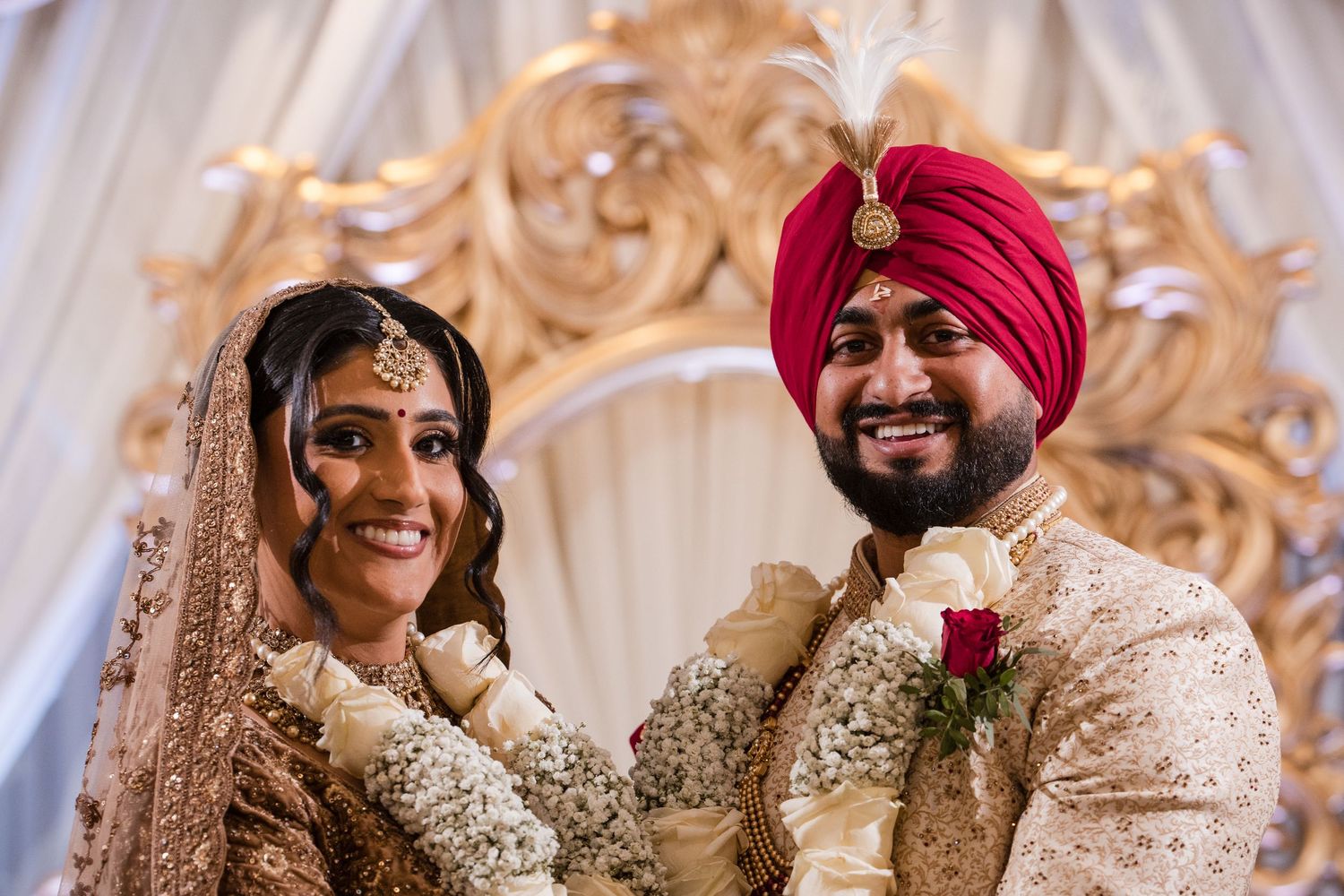 Radiant Sikh bride and groom in matching gold outfits smile together before ornate golden mandap backdrop.