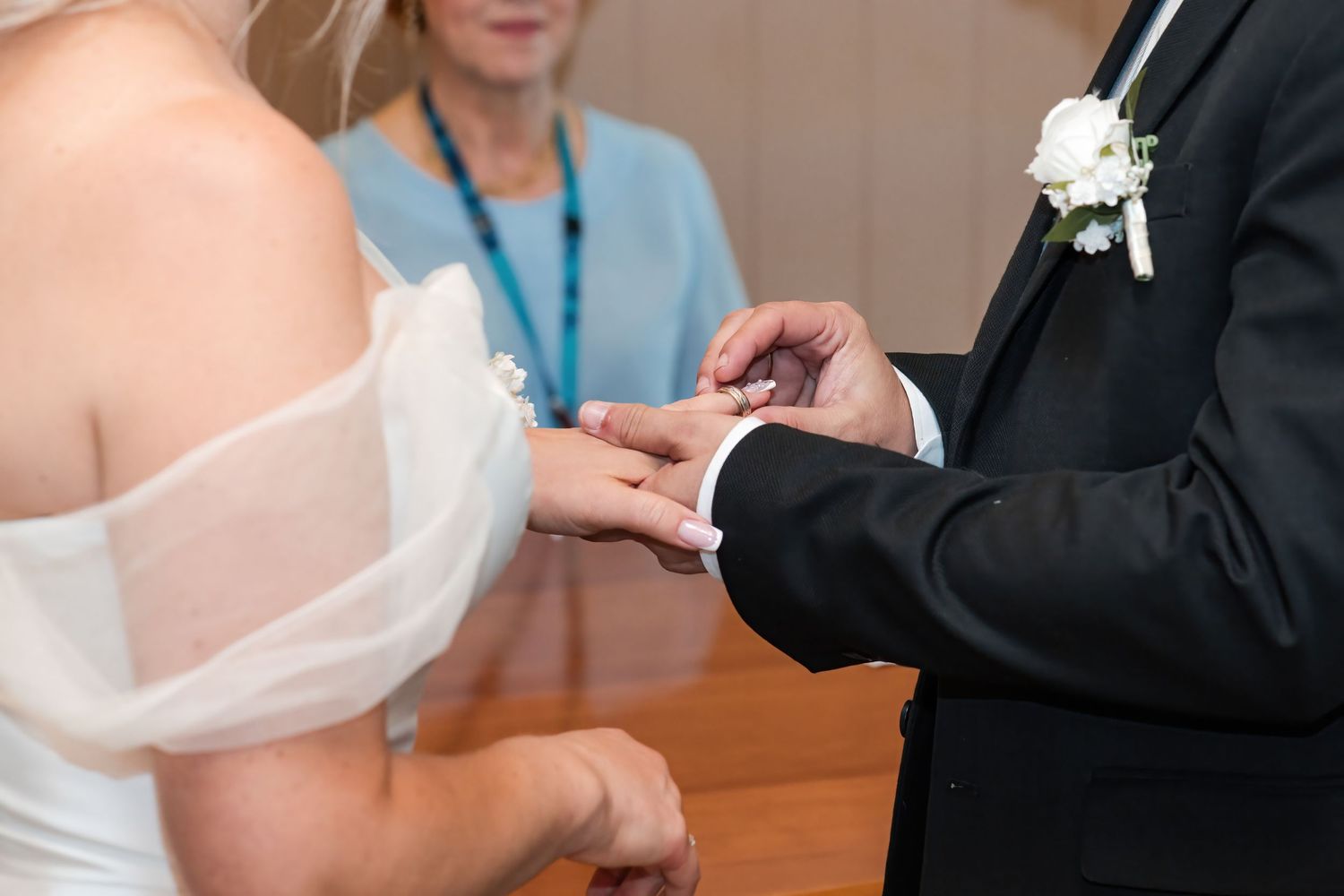 Officiant places wedding ring on brides finger during an intimate indoor wedding ceremony.