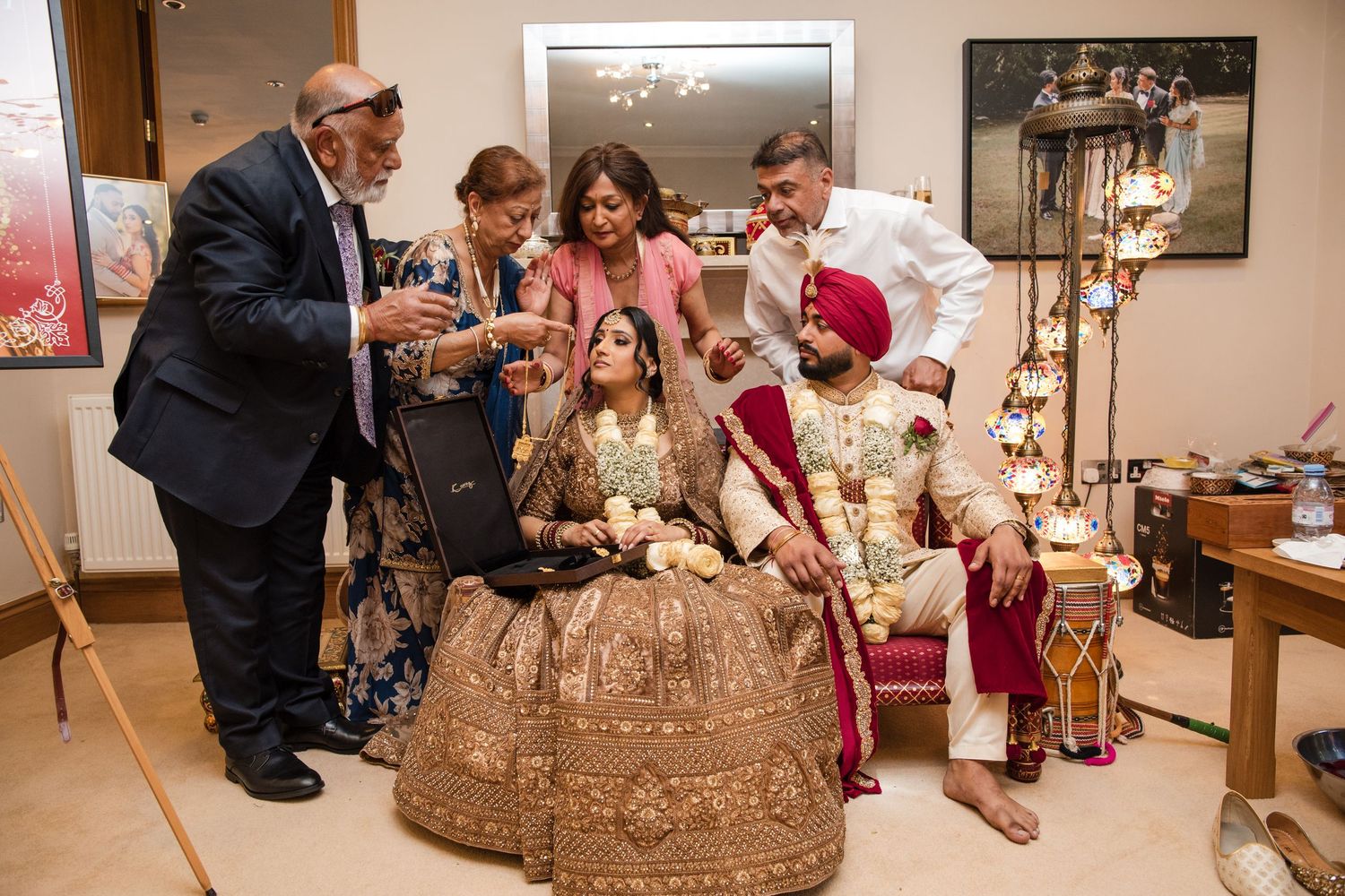 Indian bride and groom in traditional wedding attire seated while family members gather around them.