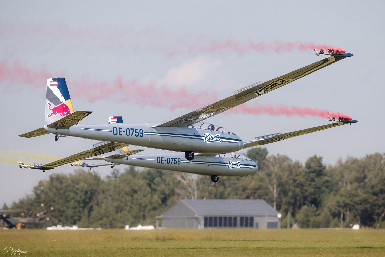 Two Red Bull gliders OE-0759 and OE-0758 taking off with colorful smoke trails.