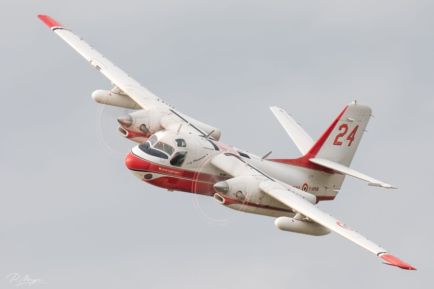 A white and red twin-engine S-2 Tracker aircraft numbered 24 flies against a cloudy sky.