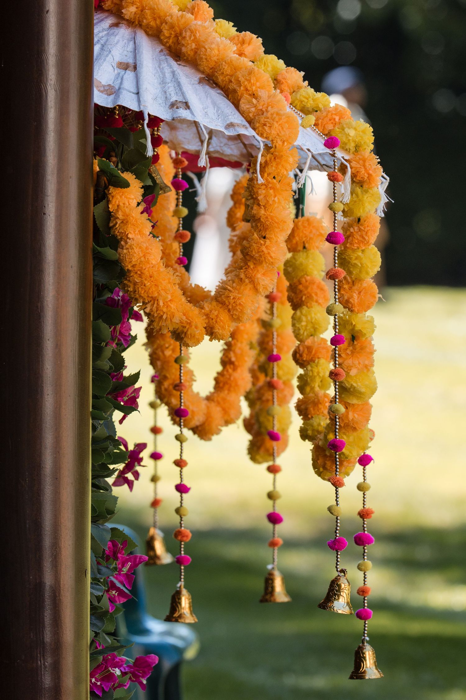 Colorful marigold flower garlands with pink pompoms and golden bells decorating an Indian wedding mandap.
