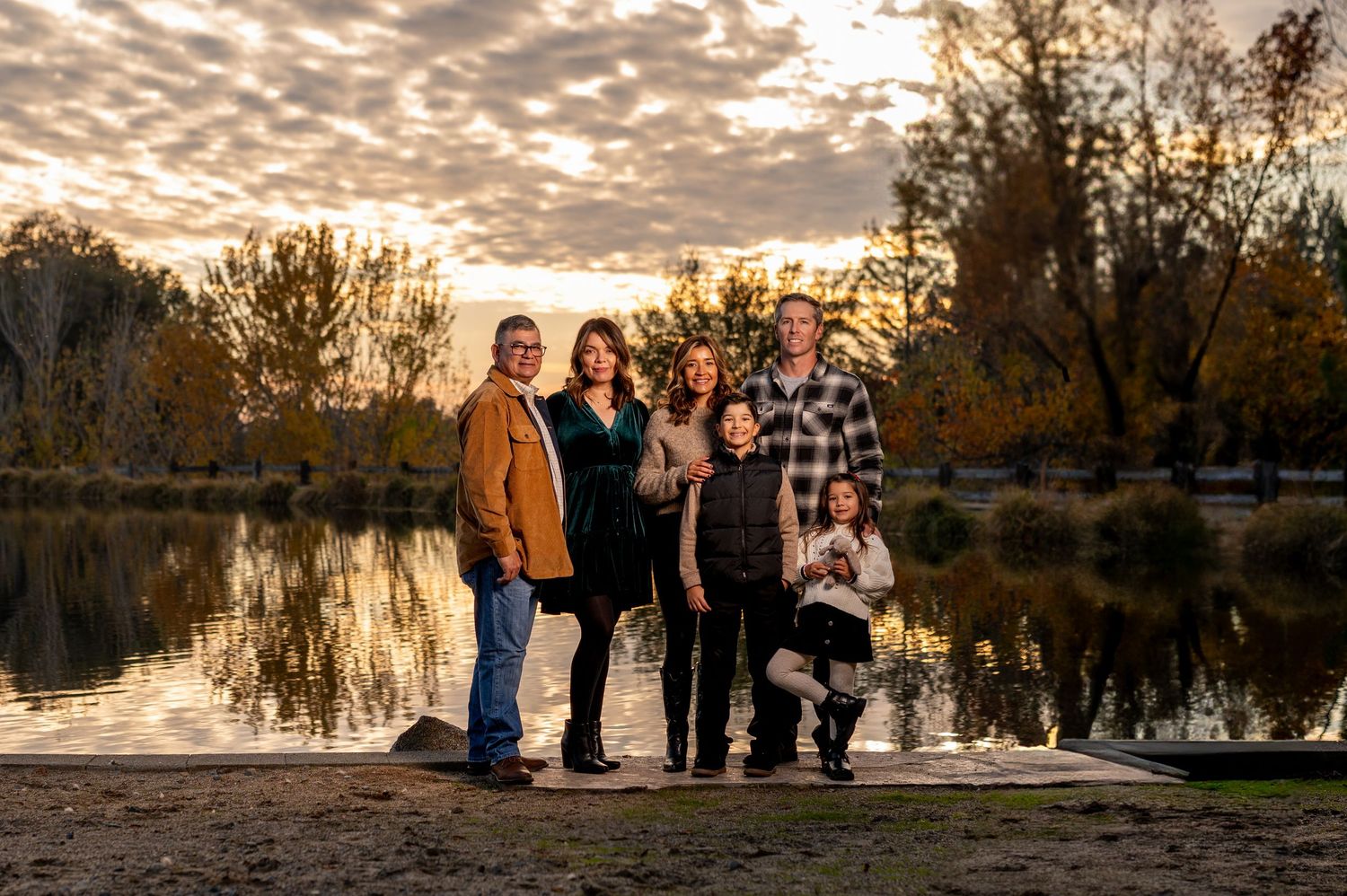 Family of six poses at Bywater Hollow Lincoln with lake and dramatic skies. Fall family session at sunset.