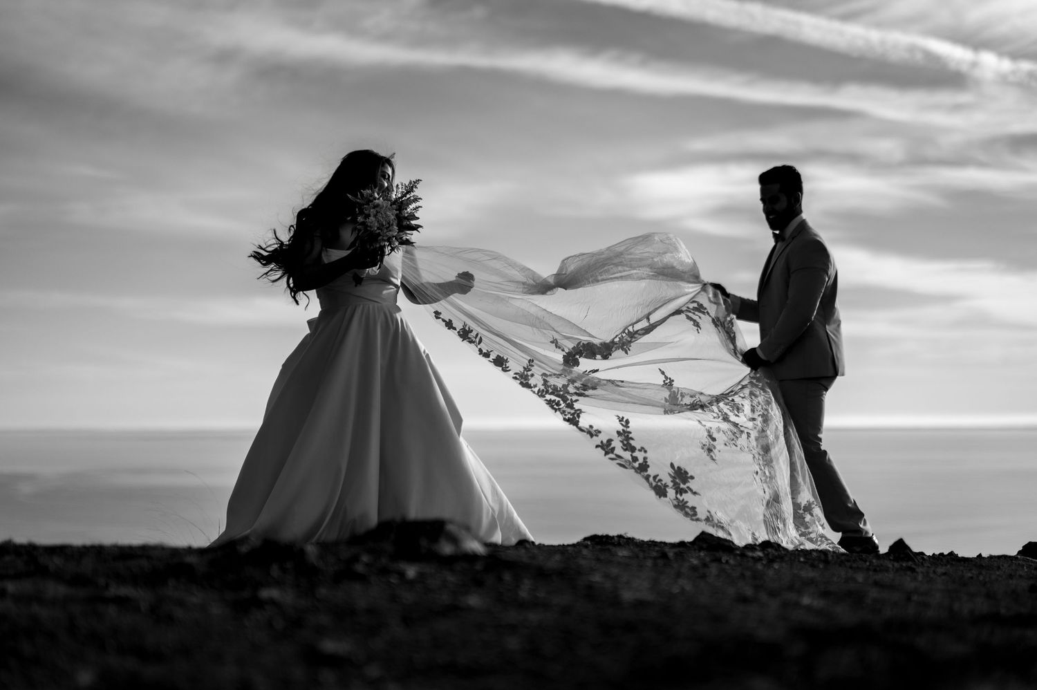 Bride and groom playing with veil on Mount Tamalpais cliffside, artistic Northern California elopement portrait by The Padillas