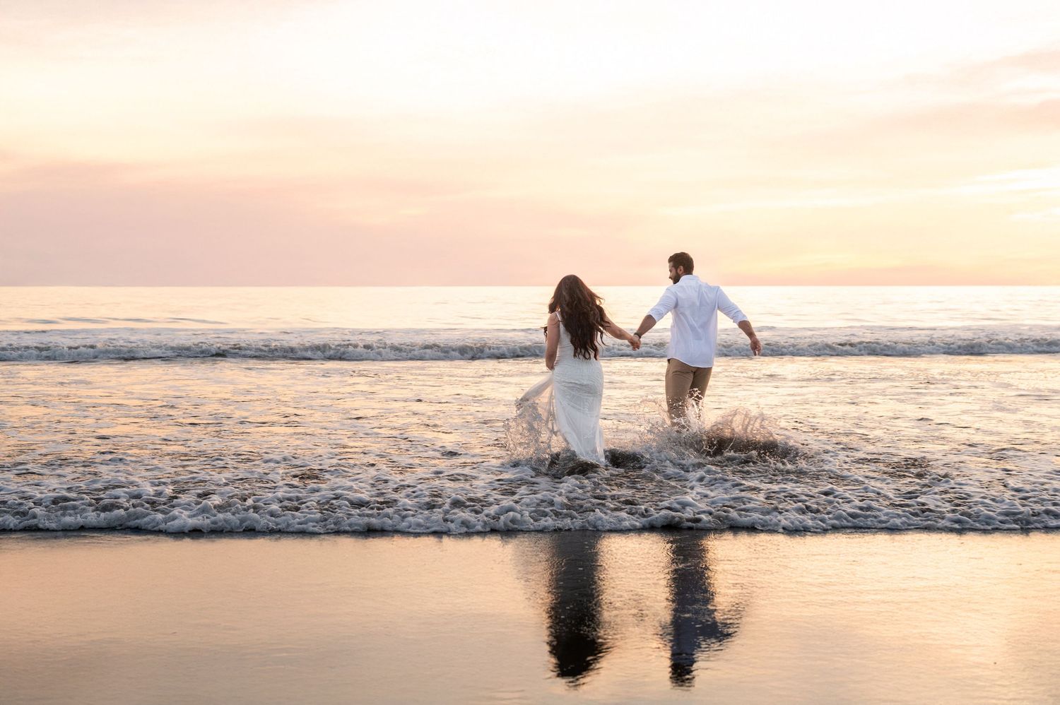 Engaged couple running into ocean waves during Stinson Beach sunset session