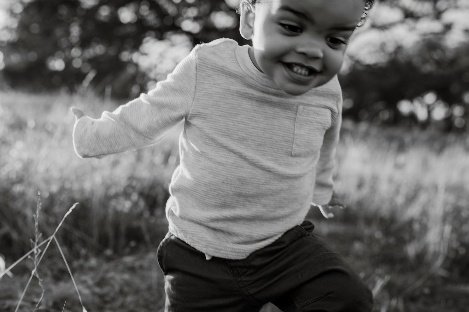 Young boy running and laughing in Folsom CA field. Lifestyle family photography capturing natural joy and play.