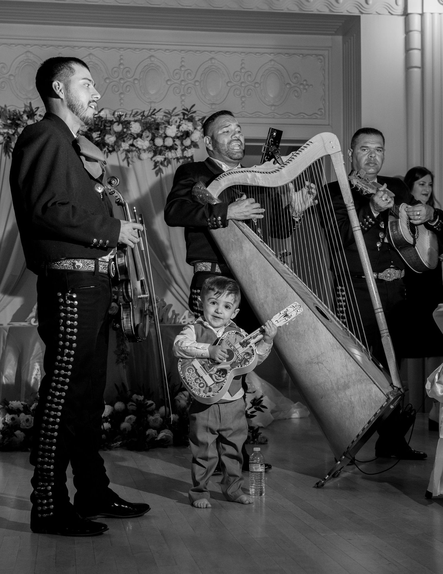 Mariachi band performing with young boy playing guitar at Sacramento Mexican wedding, candid moment captured by The Padillas.