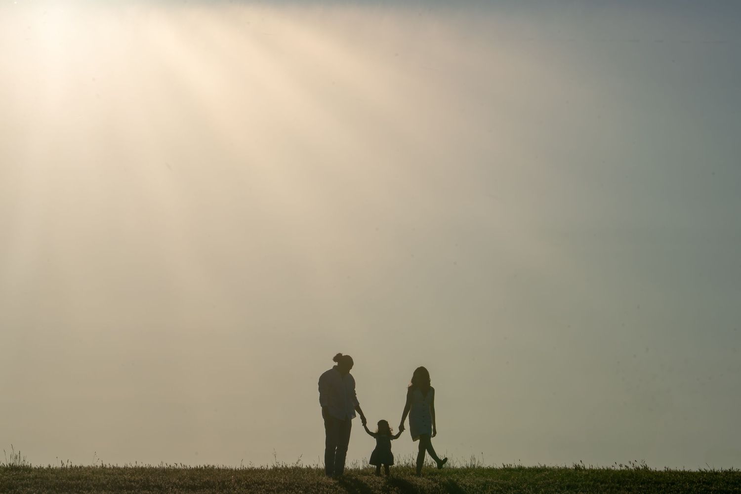Silhouette family session at Gibson Ranch, parents and child holding hands at sunset, soft dreamy light.