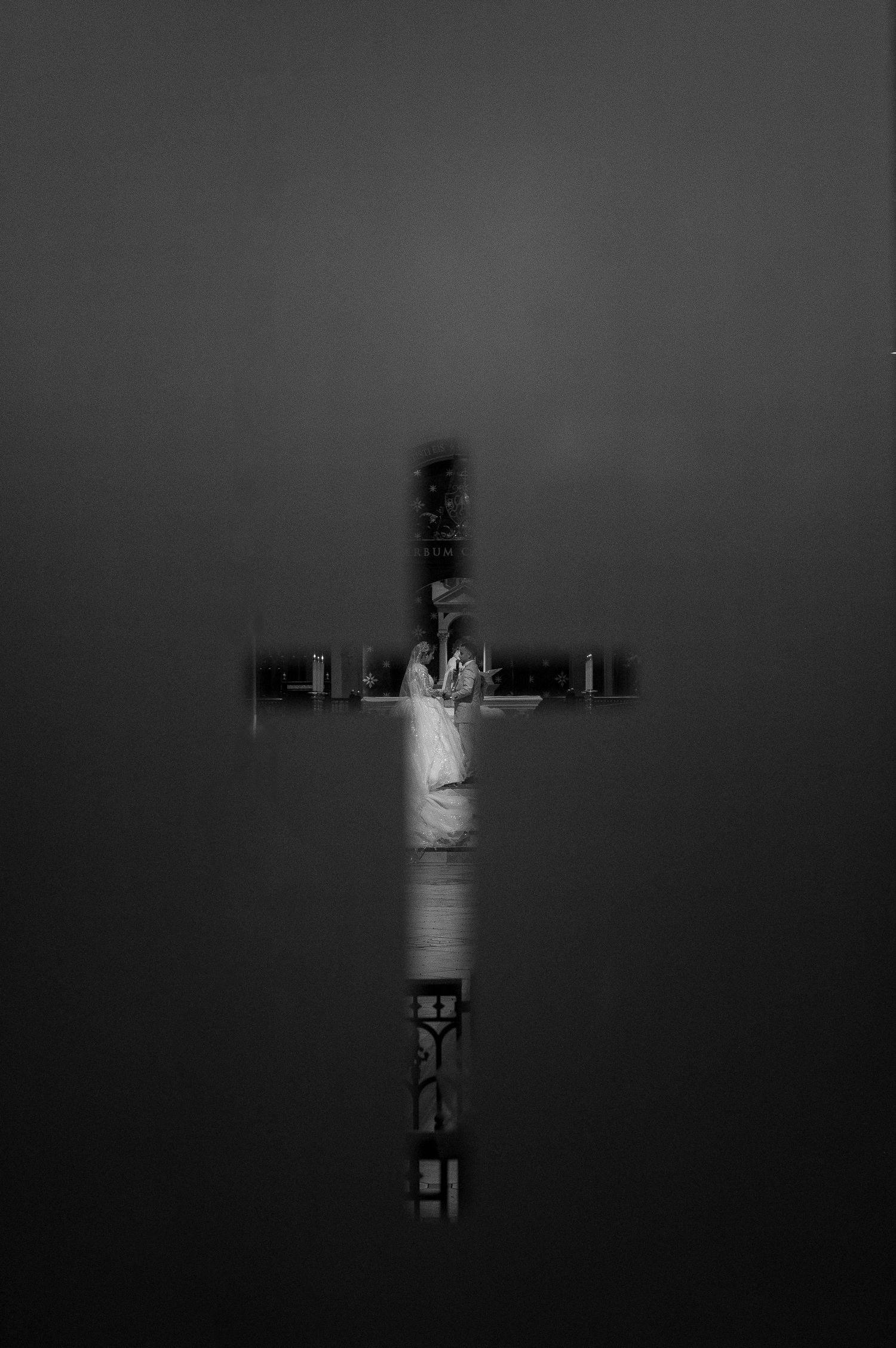 Creative wedding portrait of bride and groom through cross-shaped window at Cathedral of the Blessed Sacrament Sacramento, dramatic wedding