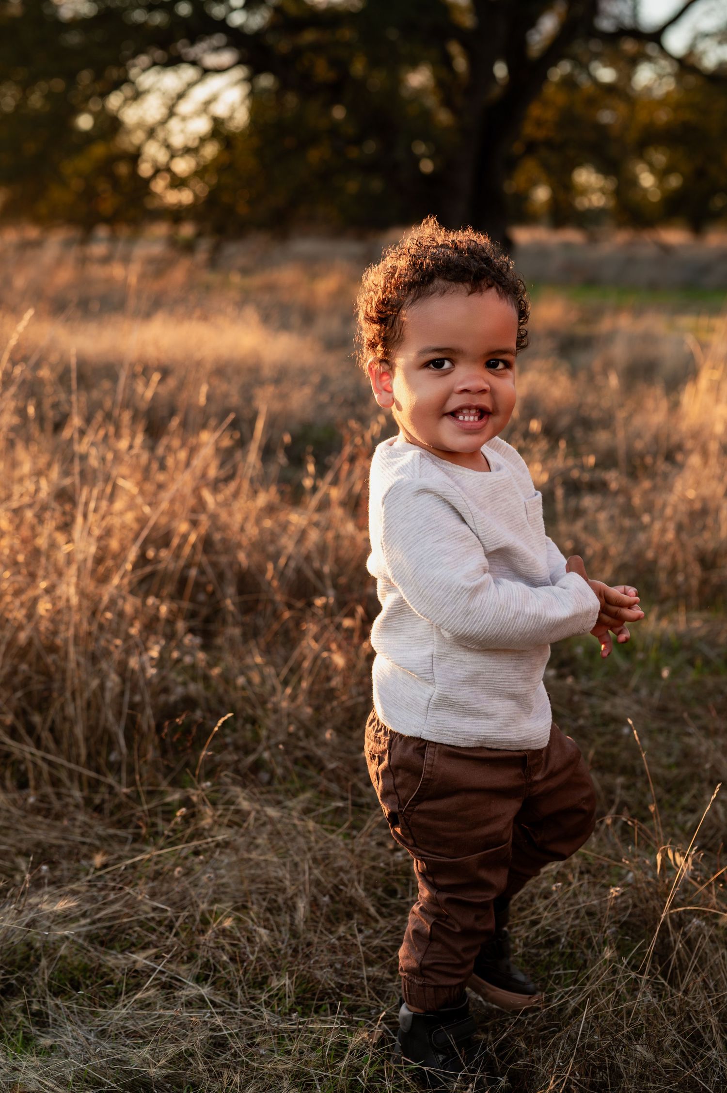 Smiling toddler standing in dry grass during golden hour family session in Folsom, California.
