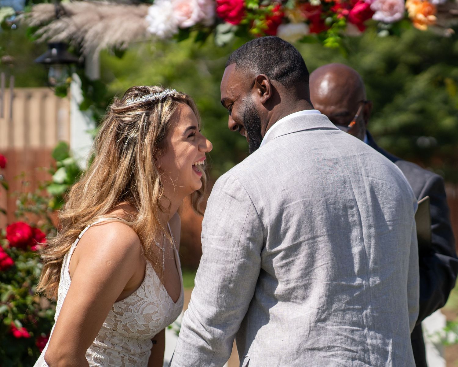 Bride and groom laughing together under colorful floral arch in Sacramento outdoor wedding, photographed by The Padillas.