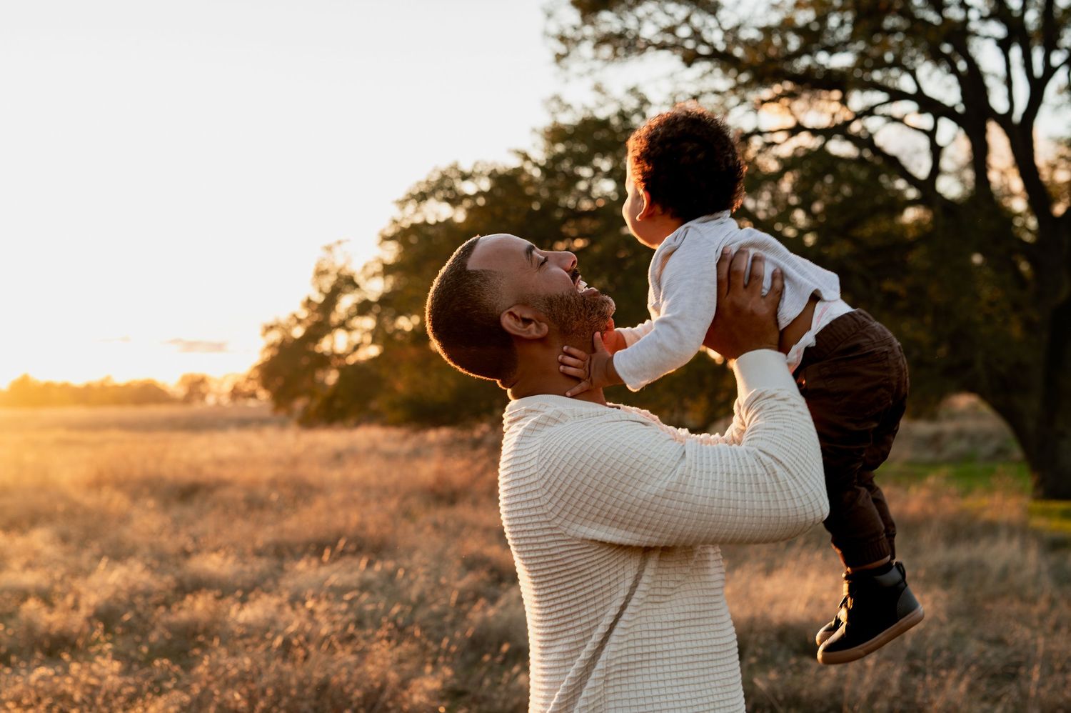 Folsom family session at golden hour, father lifting toddler in field for sweet candid moment
