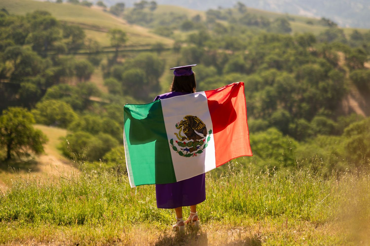 Bilingual high school graduate in purple gown holding flag