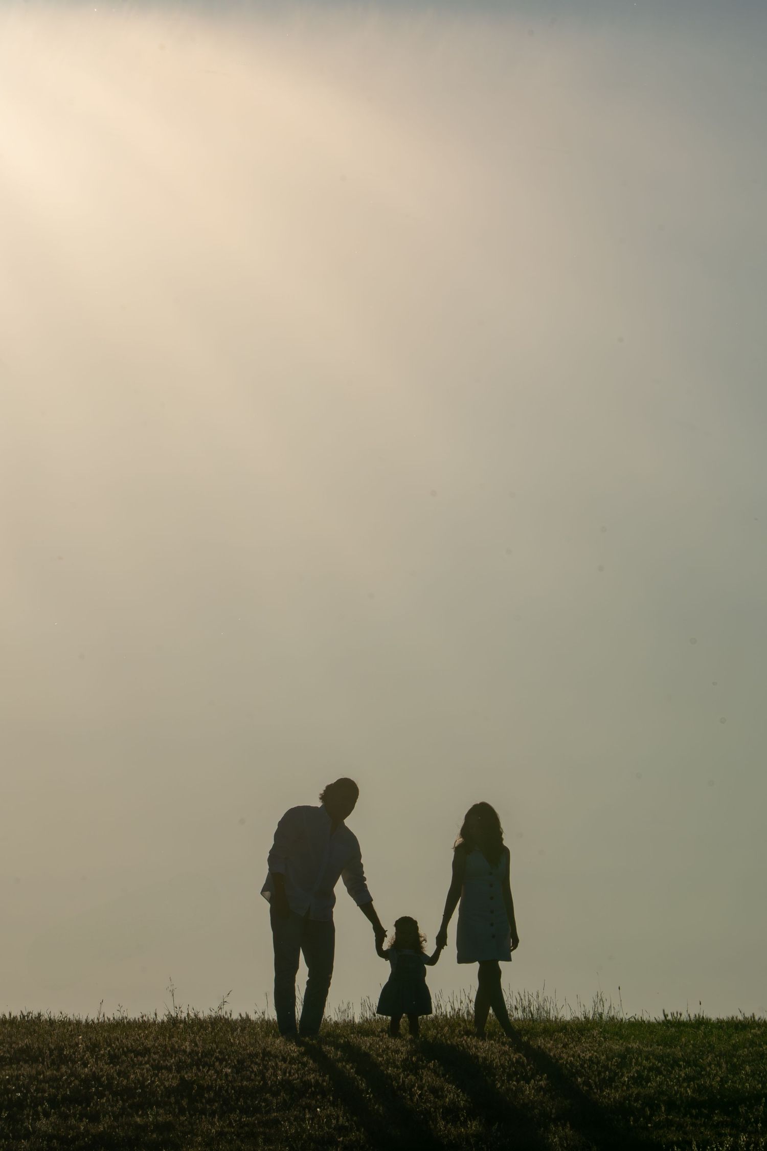 Family of three holding hands in silhouette during golden hour, outdoor family lifestyle photography in Sacramento