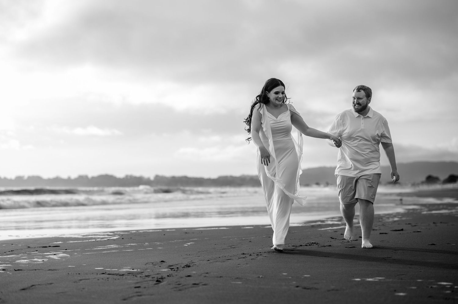 Engaged couple walking barefoot along Stinson Beach shoreline at sunset