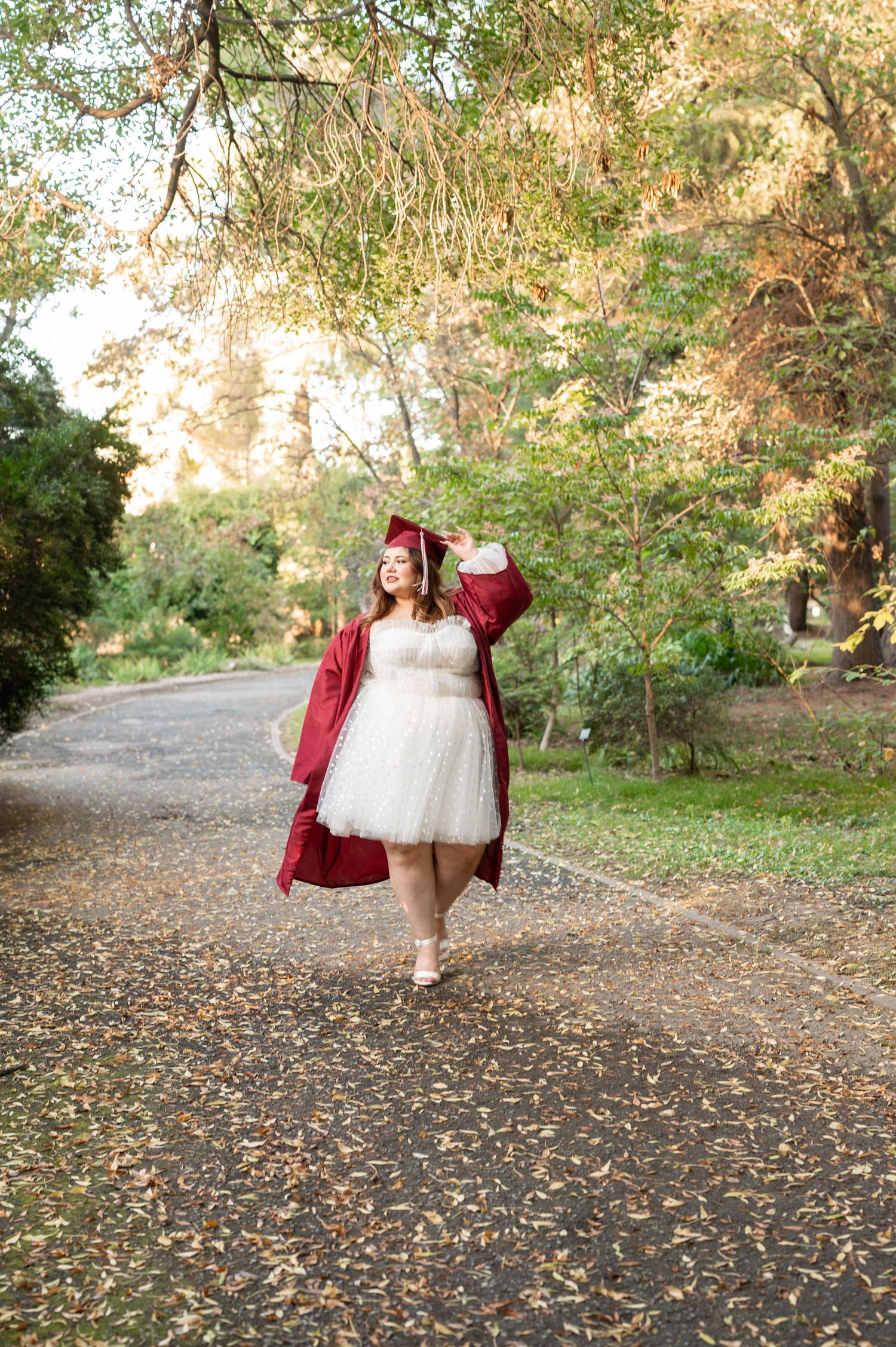 High school graduate in gown and cap walking outdoors, senior graduation portrait in Sacramento by The Padillas
