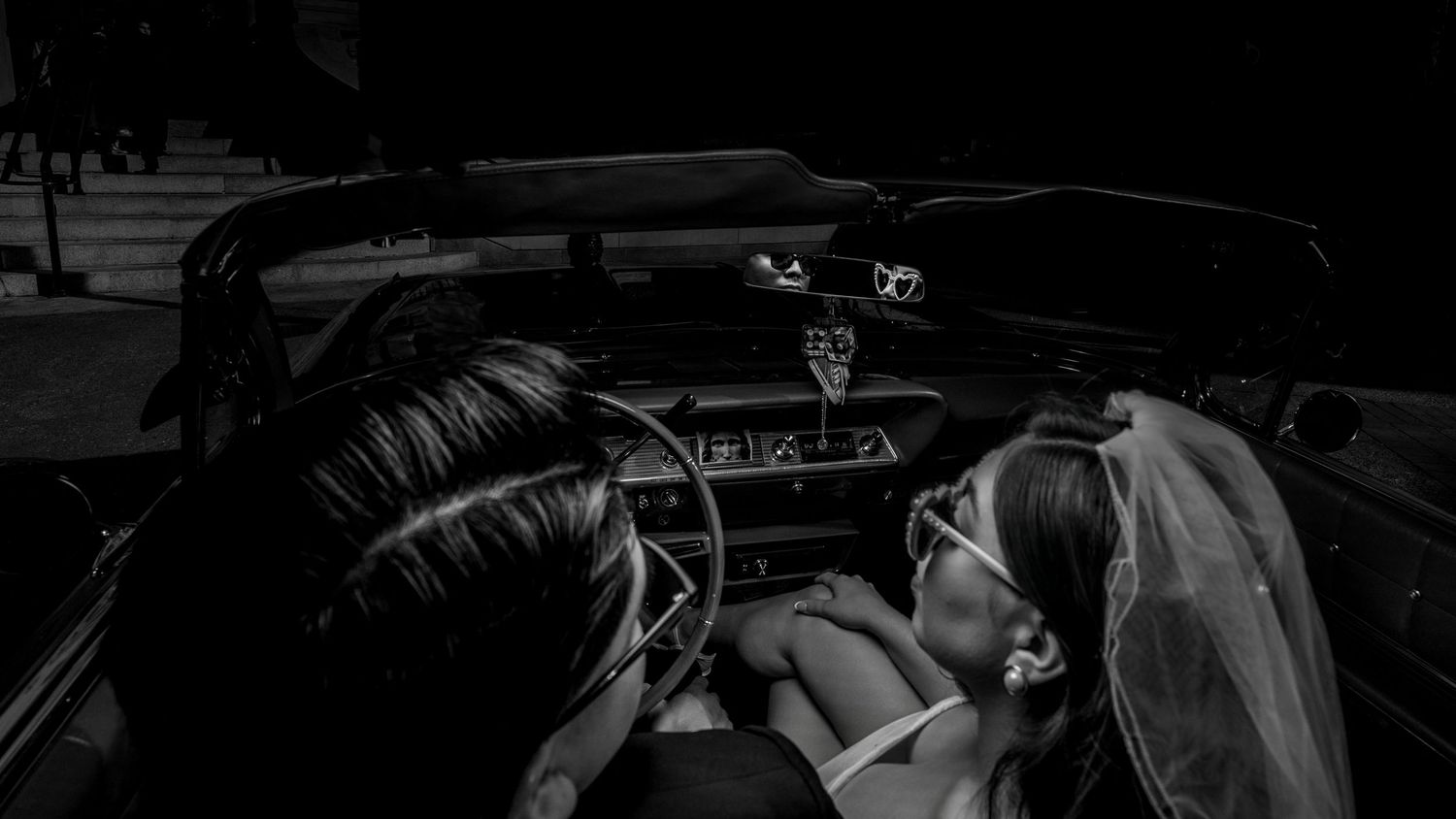 Bride and groom in vintage convertible after wedding, cinematic black and white wedding photography by The Padillas