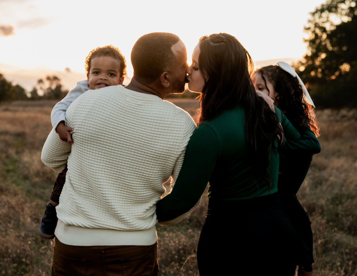 Family session at golden hour in Folsom with parents kissing and kids smiling. Natural light candid moment