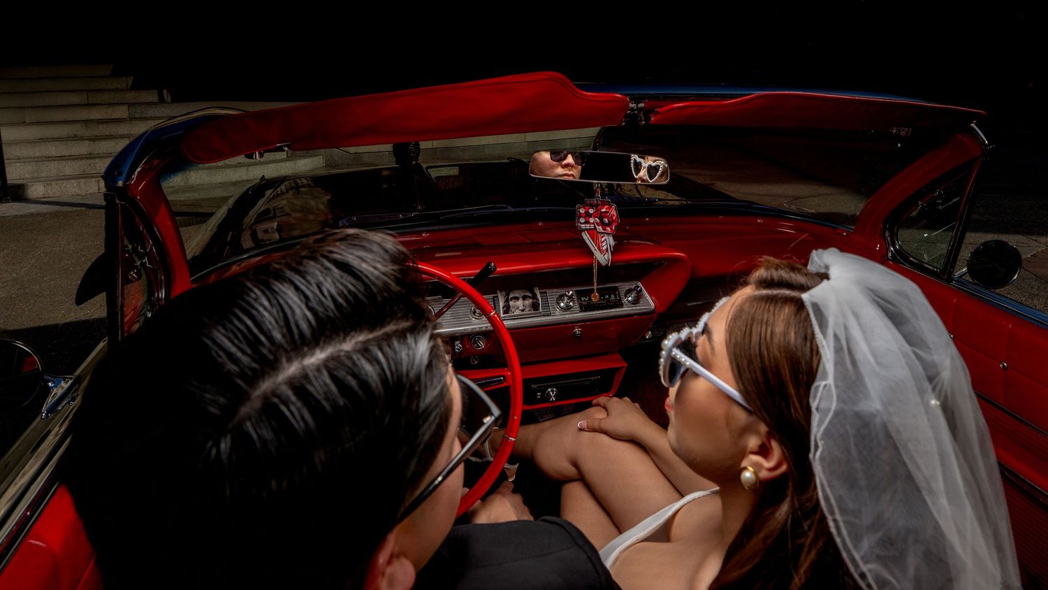 Bride and groom in vintage red convertible wearing sunglasses, close-up shot with reflection in rearview mirror, downtown Sacramento.