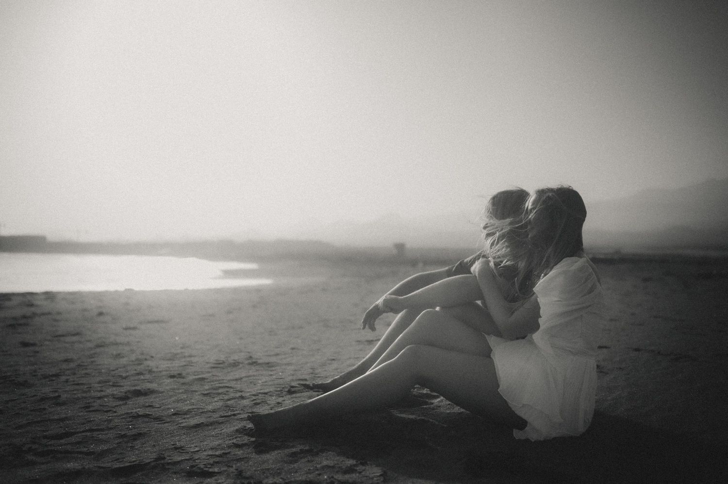 Young couple sitting side by side on Playa Tejita, she rests her head on his shoulder as they watch the sunset over the ocean, Tenerife coup