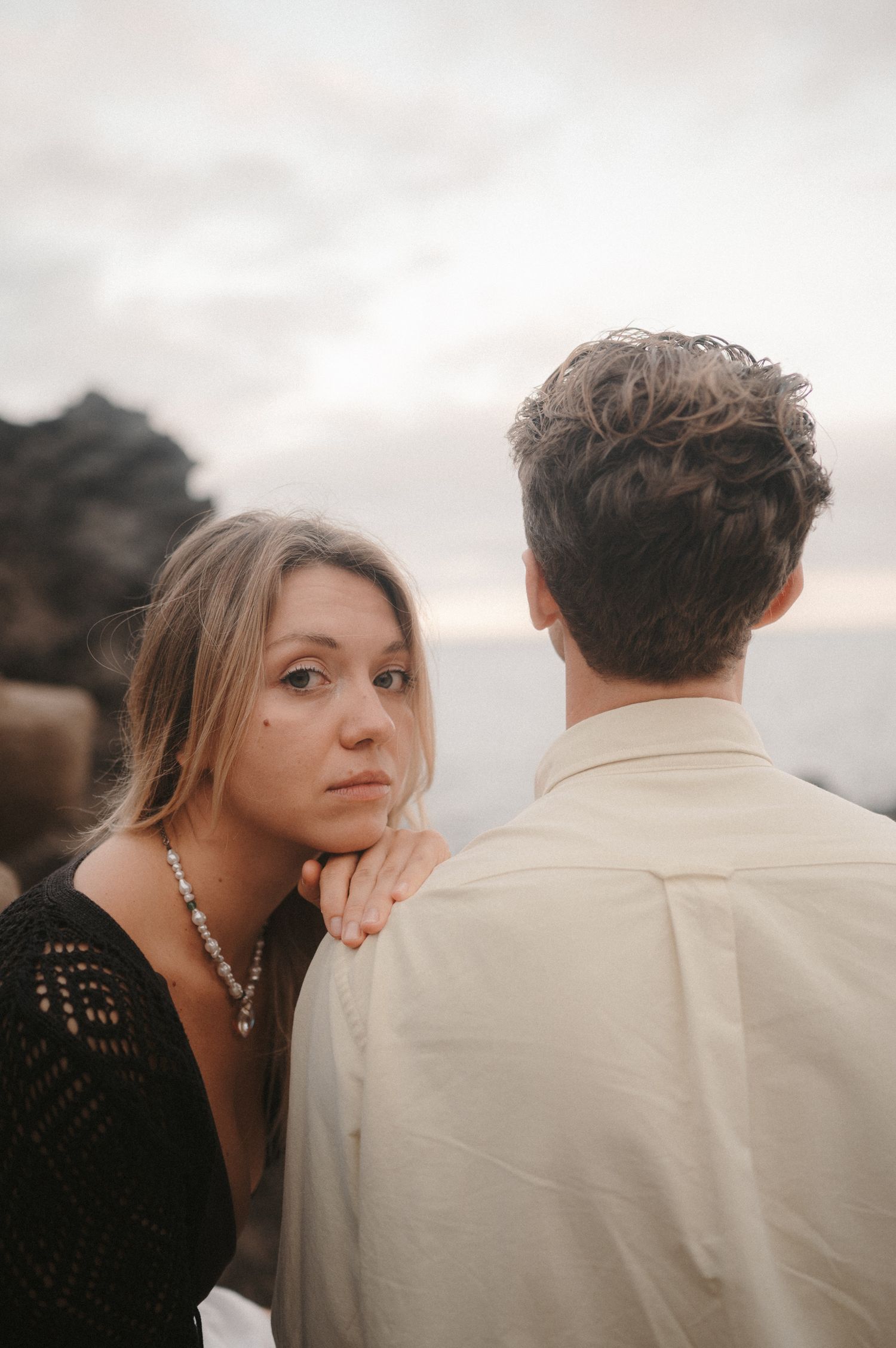 Close-up of a young couple sitting on a cliff with ocean view, sharing a romantic moment during a photoshoot in Tenerife