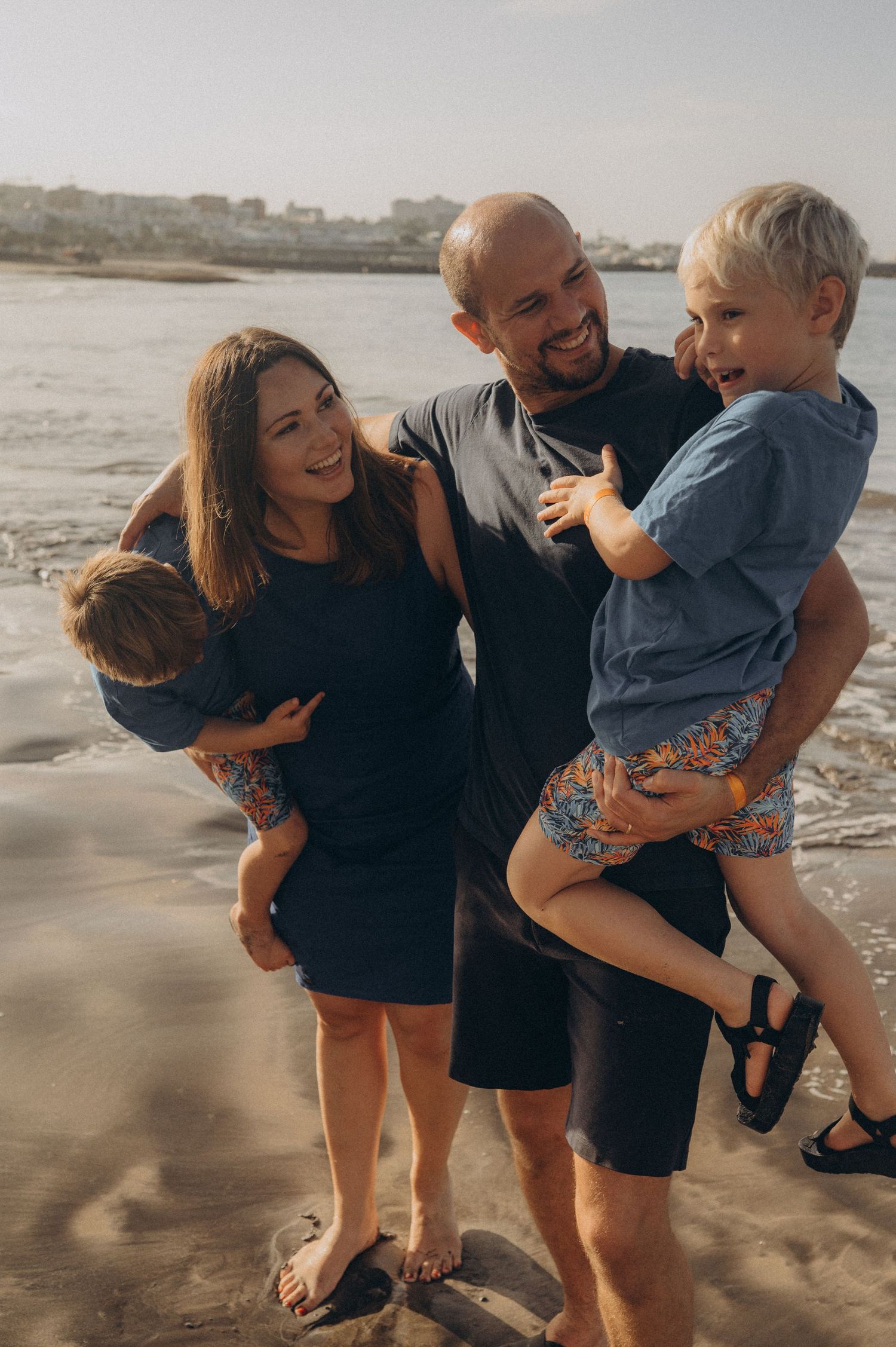 Warm morning family portrait with parents holding their children by the ocean in Tenerife