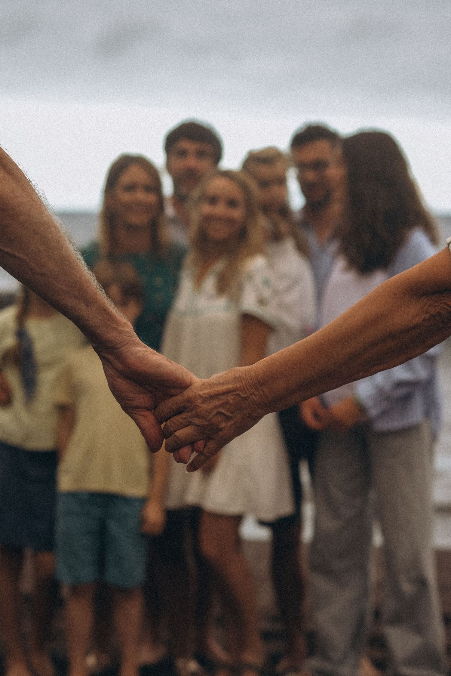 Grandparents’ outstretched hands framing their family on black sand beach at Los Refugios, Tenerife