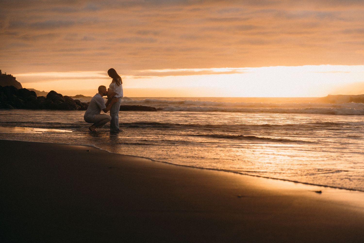 Couple sharing a romantic moment on a sandy beach at golden sunset, waves gently lapping the shore.