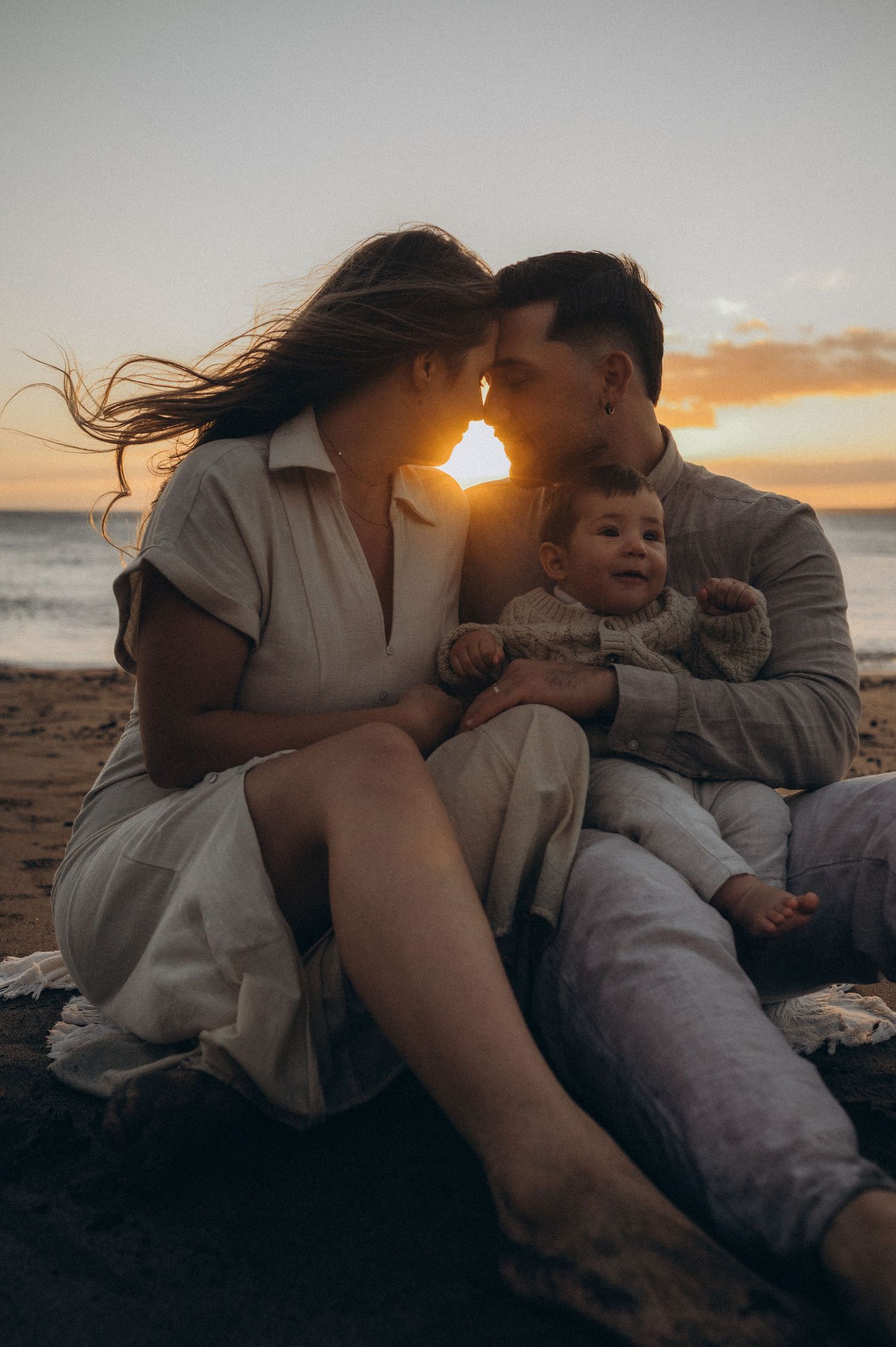 Family sharing tender moments together on a beach during golden hour at sunset.