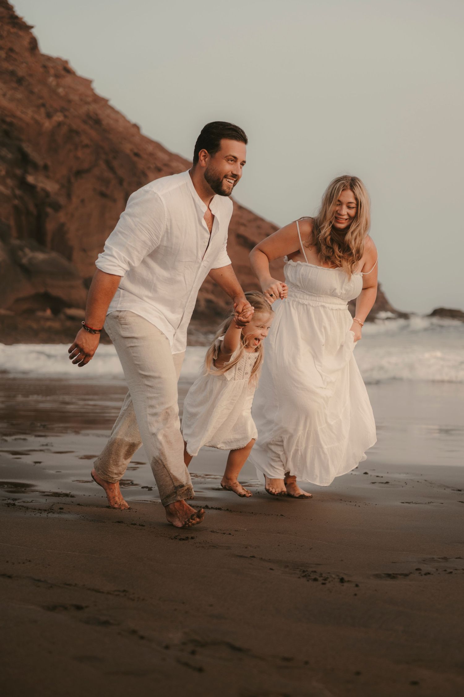 Family running together along the beach with Montaña Roja and ocean at Playa La Tejita